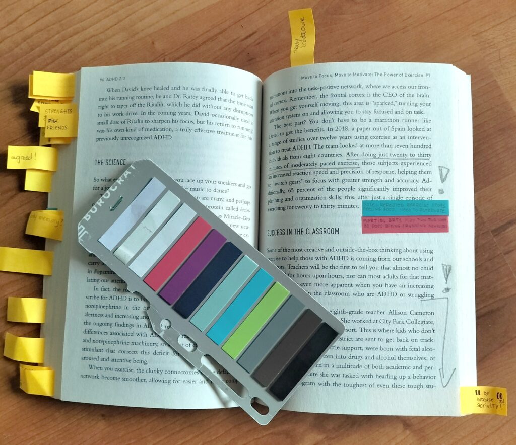 otwarta książka ADHD 2.0 z doklejonymi kolorowymi karteczkami i oznaczeniami zrobionymi ołówkiem